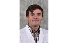 Tanner Movick smiles in his white coat in front of a gray background. 